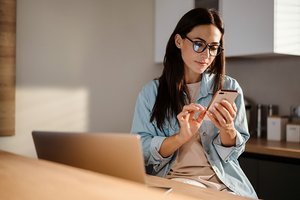 Photograph of a seated woman using her mobile phone and laptop computer to search for information.
