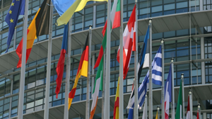 Multiple national flags waving in front of a modern building.