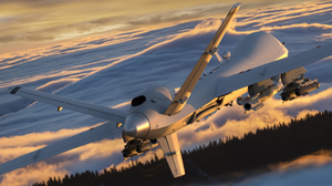 Military drone flying over a snowy mountain range with a forest below.