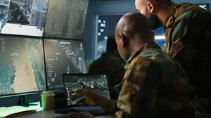 Military personnel in uniform analyze data on laptops and monitors.