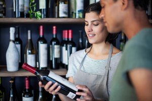 Wine store coworkers reading wine bottle label while standing indoors.