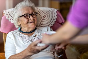 A nurse handing something to a smiling elderly lady sitting on a chair.
