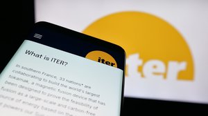 Photograph of a hand-held device displaying a description of the ITER Organization, with the ITER website in the background