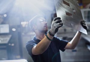 Photograph of a young man, focused on his work examining a part in a steel factory.
