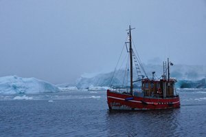 Photograph of a mid-sized shipping boat on a flat sea with ice floats in the background. 