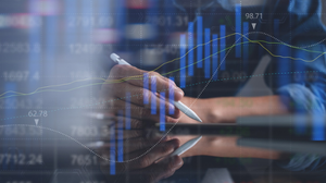  Photograph in soft focus of workers' hands in an office environment, one holding a pen, with an overlay of onscreen data.
