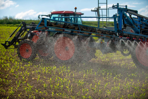 An agricultural boom sprayer attached to a tractor applying fertilisers across a field of young crops.