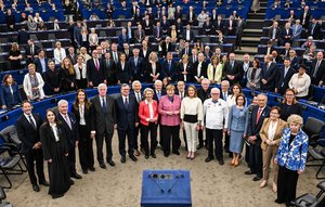Photograph of the conferral ceremony for the European Order of Merit, showing the laureates standing in a semicircle in the European Parliament plenary chamber