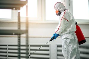 Professional disinfector in protective suit with chemical sprayer and sterilisation equipment.