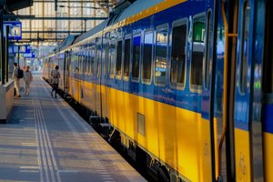 Train waiting at a railway station with three blurred figures on the platform.