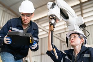Engineers using a robotic arm in an industrial setting for automation development in a manufacturing facility.
