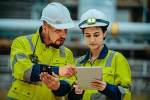 Photograph of two workers in safety gear, a mentor teaching a trainee how to operate a machine