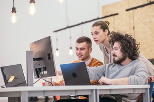 Photograph of three young workers, looking enthusiastic about content on the screens on their desks.
