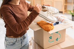 Young woman packing shoes into a recycling box in a bedroom.