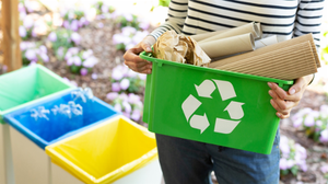 Close-up of a green basket with a recycling symbol with papers held by a woman