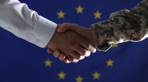 Photograph of a civilian and a soldier shaking hands against an EU flag