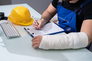 Picture of a worker with an injured left arm filling in paperwork for the insurance