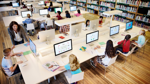 School children and their teacher working on computer screens in a library