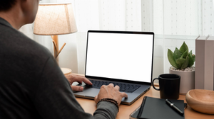 Man typing on laptop with blank screen mockup in cozy home office workspace