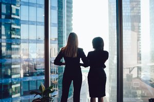 Back view of two women in business suits looking out of the window to nearby skyscrapers