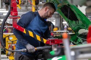A mechanic in workwear uses tools in a car workshop.