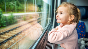 Happy little girl looking out train window outside, while it is moving.