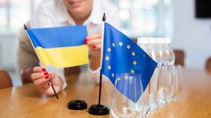 Young woman in business clothes puts small European Union and Ukraine flags on table in office