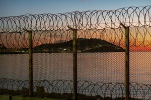  Photo of Ceuta with sea in front of it, seen through a fortified fence on the Moroccan coastline.