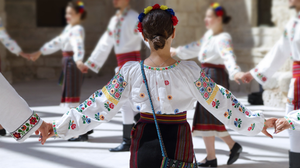 Female dancers wearing one of the traditional folk costumes from Romania dancing in a circle while holding hands