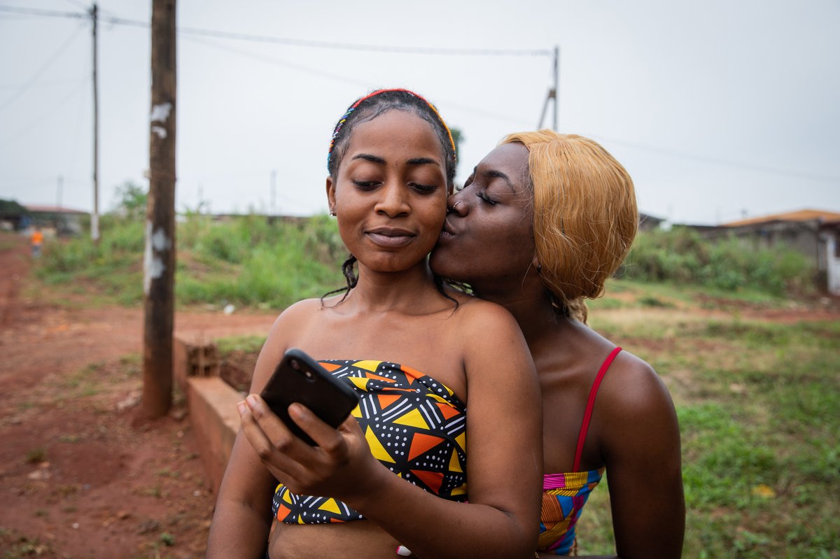 Two African women sharing an intimate moment outdoors, one kissing the other on the cheek.