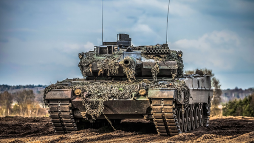A camouflaged military tank on a muddy field.