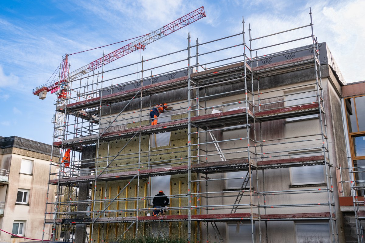Photograph of a fa&ccedil;ade of a social housing building, covered in scaffolding, showing before and after thermal renovation.