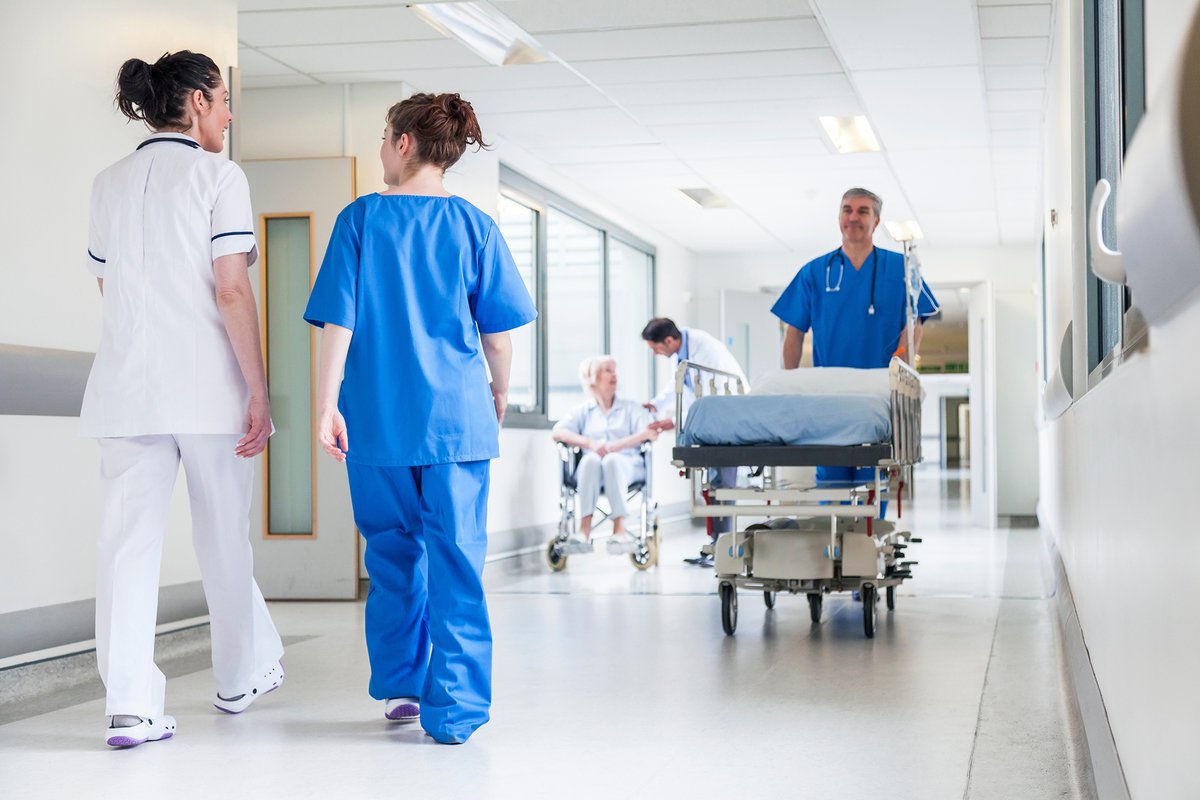 Four healthcare professionals and a patient in a typical hospital corridor.