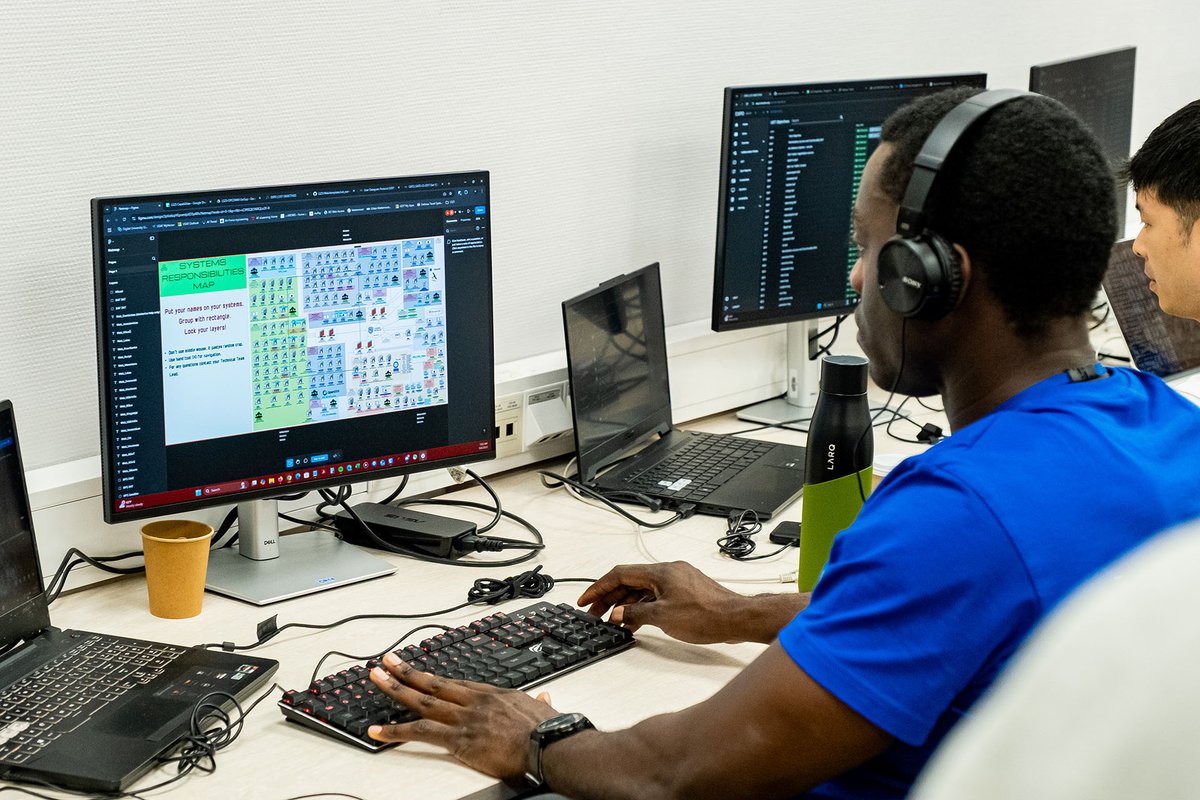 African man wearing headphones, looking at a screen, typing on a keyboard in a working environment