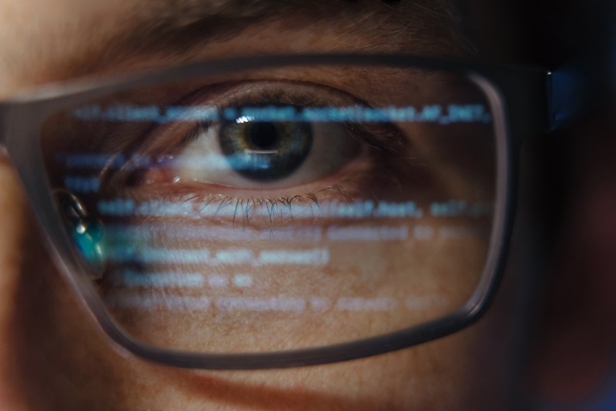 Extreme close-up of a programmer's or a software engineer's eye with computer code reflecting on glasses