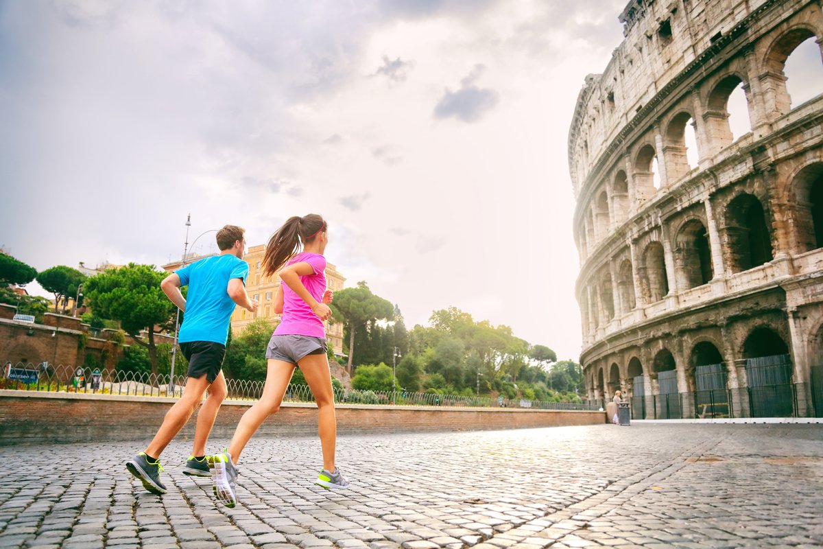 Photograph of two people running across a cobbled street towards an ancient monument (coliseum)