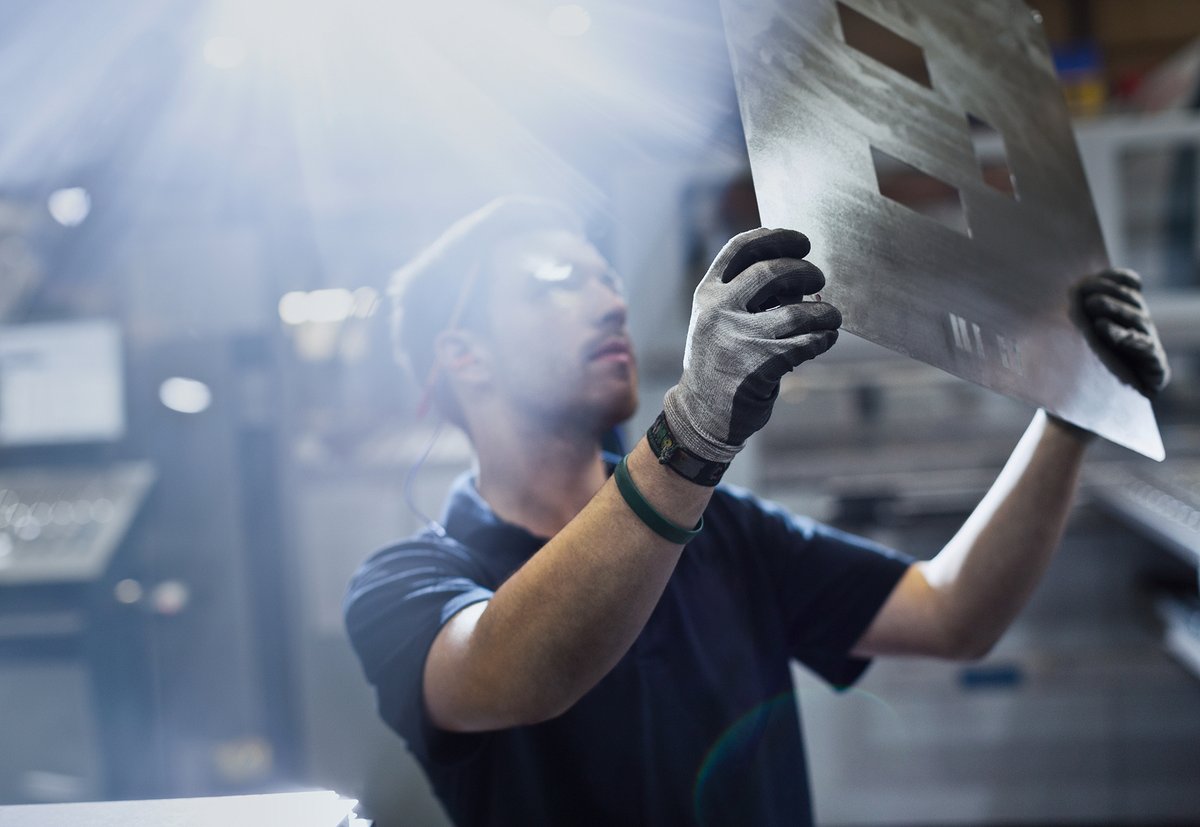 Photograph of a young man, focused on his work examining a part in a steel factory.