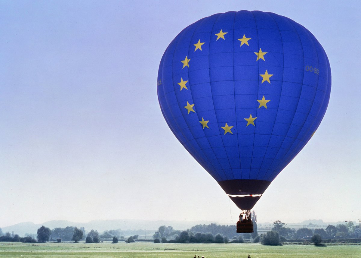 Photograph of a hot air balloon with the European emblem, rising above a field