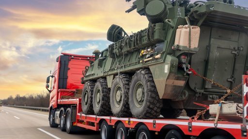 Photograph of a truck carrying an armoured personnel carrier striker, seen from behind