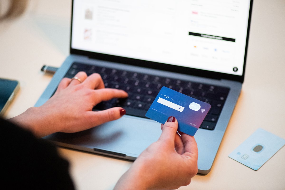 A person holding an upturned bank card while shopping on a laptop
