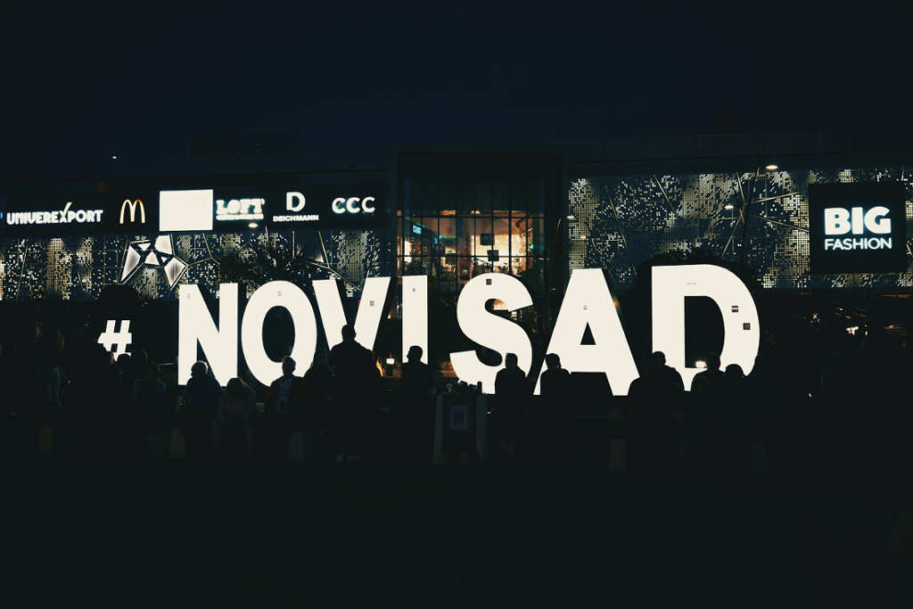 Photograph taken at night of a commemorative gathering of citizens in Novi Sad, in front of the illuminated "NOVI SAD" letters