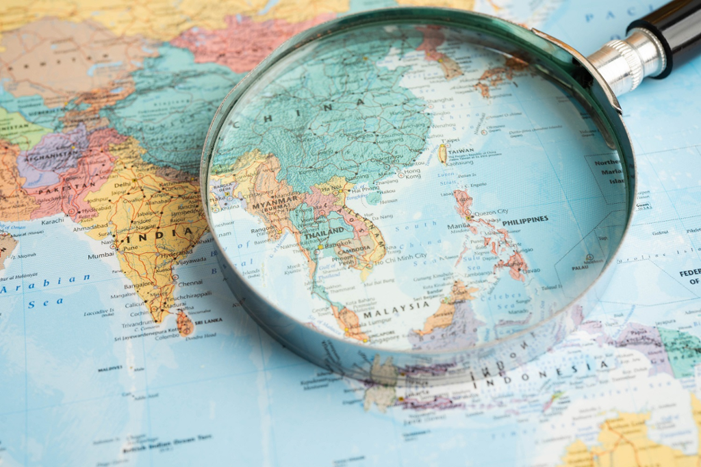 Photograph of a magnifying glass sitting on top of a world map, South-East Asia in focus