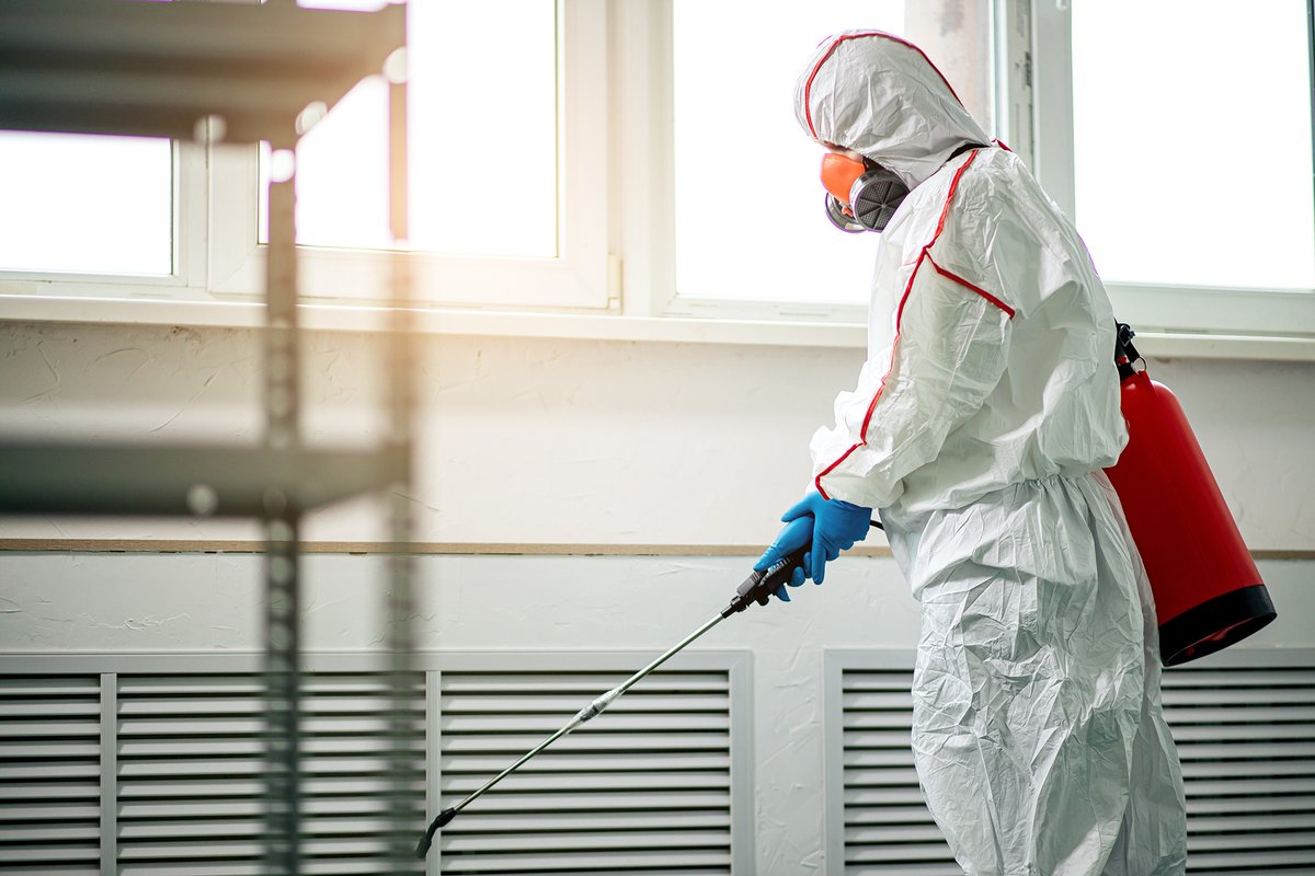 Professional disinfector in protective suit with chemical sprayer and sterilisation equipment.