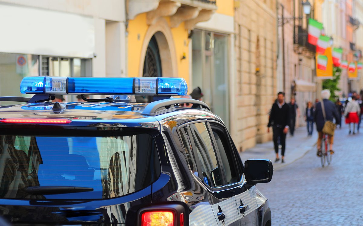 Photograph of a police car patrolling a city street, pedestrians and cyclist in the background.