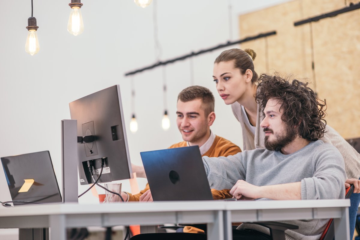 Photograph of three young workers, looking enthusiastic about content on the screens on their desks.