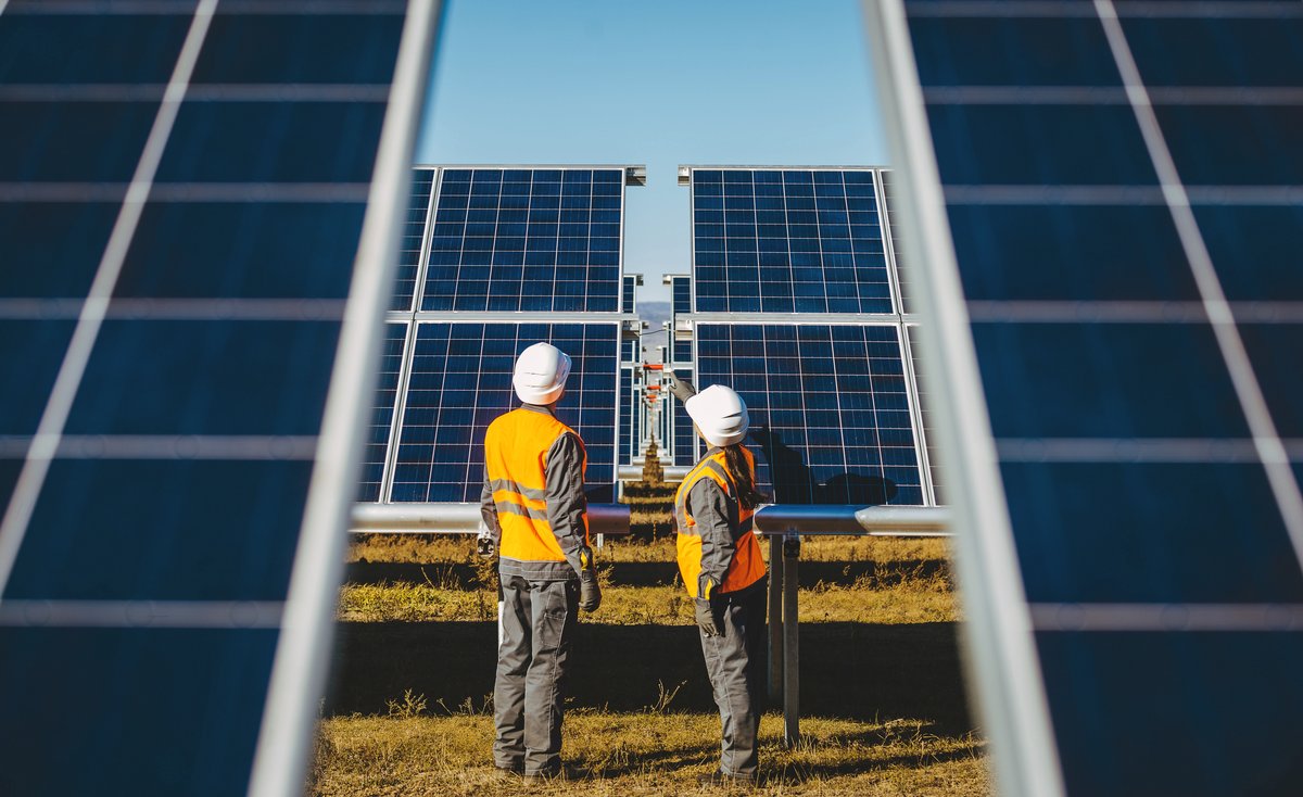 Photograph of two construction engineers wearing orange reflective vests in a solar panel field.
