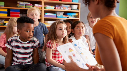 Group Of Elementary School Pupils Sitting On Floor Listening To Female Teacher Read Story