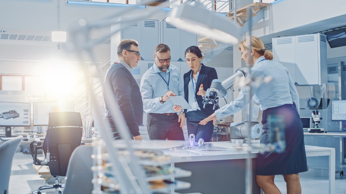 Diverse Team of Industrial Robotics Engineers Gathered Around Table With Robot Arm