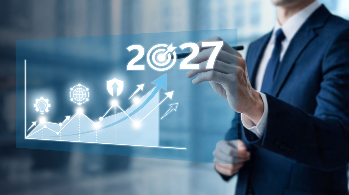 This photograph shows a businessman in a suit pointing to a digital projection of a business growth graph with the year 2027 prominently displayed.