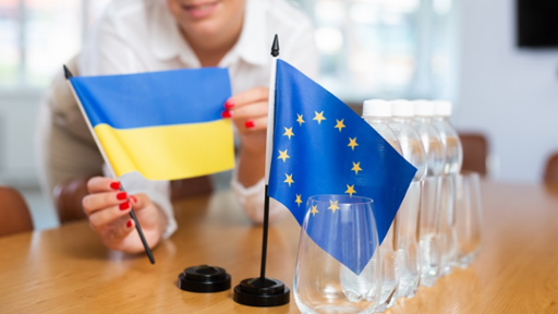 Young woman in business clothes puts small European Union and Ukraine flags on table in office